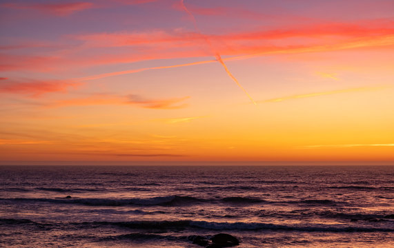 Beautiful dusk sky over the ocean, with red, orange and yellow gradient sky and reflections on the ocean waves below.