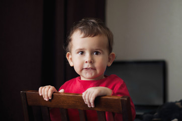 Cute 2 year old boy in a red shirt posing standing on a chair.