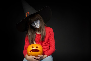 Serious Halloween witch holding Jack O'Lantern pumpkin looking at camera