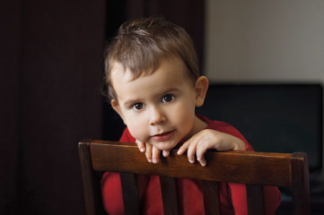 Cute 2 year old boy in a red shirt posing standing on a chair.