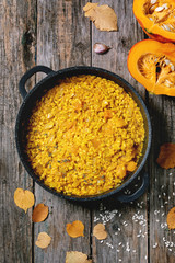 Traditional vegetarian pumpkin risotto italian dish in iron pan over old wooden background with ingredients and autumn leaves above. Flat lay, space