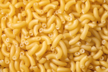 Heap of raw uncooked italian pasta coquillettes over brown texture background. Flat lay. Food background. Macro, close up