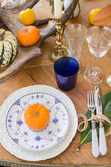 Luxurious elegant wedding decor in autumn style. Wooden vintage table setting with ceramic plates and silver cutlery. Fresh flowers in a vase, orange pumpkins, deer horns and candles. Romantic dinner.