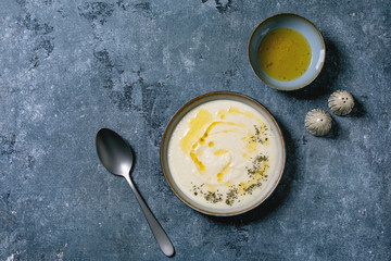 Parsnip or cauliflower cream soup in ceramic bowl with butter sauce and herbs over blue texture background. Flat lay, space