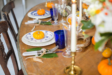 Luxurious elegant wedding decor in autumn style. Wooden vintage table setting with ceramic plates and silver cutlery. Fresh flowers in a vase, orange pumpkins, deer horns and candles. Romantic dinner.