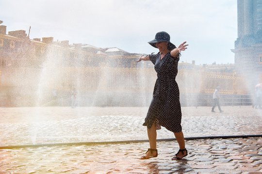Happy girl in dress and hat in a spray of water on a sunny summer day, Versailles, France