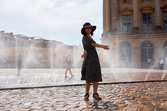 Happy girl in dress and hat in a spray of water on a sunny summer day, Versailles, France