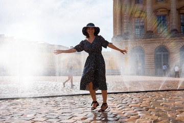 Happy girl in dress and hat in a spray of water on a sunny summer day, Versailles, France