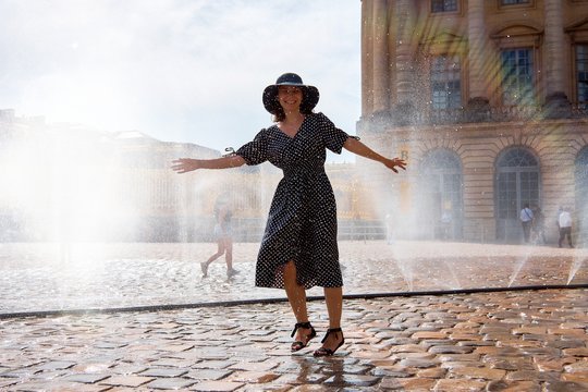Happy girl in dress and hat in a spray of water on a sunny summer day, Versailles, France