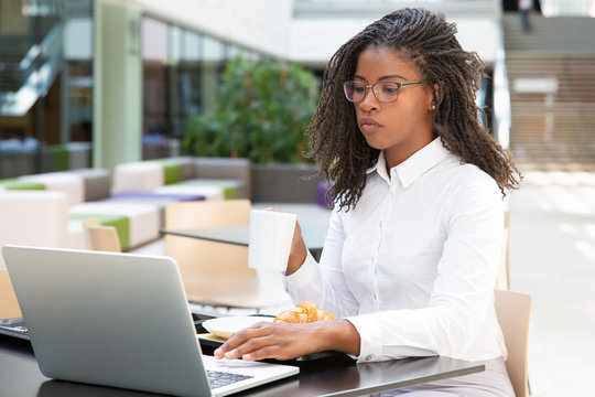 Focused businesswoman drinking coffee while working on project in cafe. Business woman having breakfast and using laptop. Business morning concept