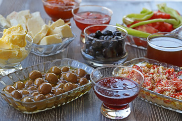 Breakfast with cheese, tomatoes, olives, butter and jam on wooden table.