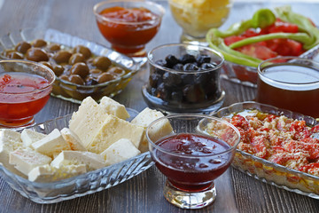 Breakfast with cheese, tomatoes, olives, butter and jam on wooden table.