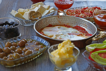 Breakfast with cheese, tomatoes, olives, butter and jam on wooden table.
