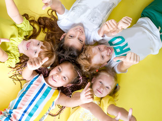 A group of fashionable children lie on a yellow background looking at the camera with their thumb up. Childhood, happy children