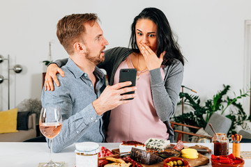 couple at home amazed and surprised by something they have just seen on their mobile phone. communication, wireless technology, social media concept