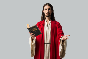 Fototapeta premium handsome man gesturing and holding holy bible isolated on grey
