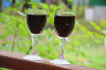 Two glasses of wine pouring wine from a bottle on a background of green foliage. Autumn concept with red wine glasses, wine bottles, vineyard landscape and grapes in nature.