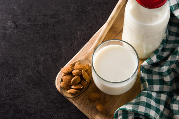 Almond milk in glass and bottle on black background. Copy space