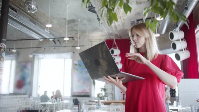 Girl in cafe standing with laptop is a make work plan, chat with friends in laptop