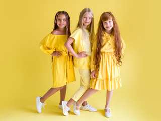 Three beautiful girls of 7 years old in yellow clothes with long hair posing looking at the camera on a yellow background. Kids in trendy stylish clothes.