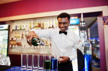 African american bartender at bar making coctails on shots. Alcoholic beverage preparation.