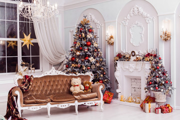 Tall Christmas tree decorated with red ornaments, baroque sofa, stucco wall in spacious light room in baroque style.