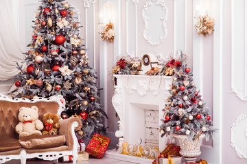 Tall Christmas tree decorated with red ornaments, baroque sofa, stucco wall in spacious light room in baroque style.