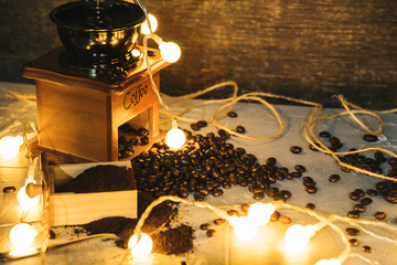 coffee grinder and coffee beans with ground powder on table. Side view Hot coffee and pastries on old kitchen table rustic. with led string lights.