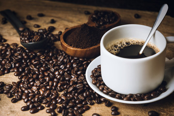 Top view Hot black coffee on a old kitchen table. background concept Coffee cup and and coffee beans with ground powder on wooden table. Coffee beans spread on the table.