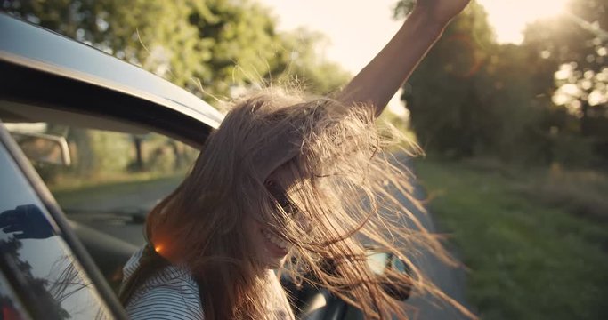 Happy young lady in eyeglasses looking out of car window and enjoying ride, wind fluttering hair, joy