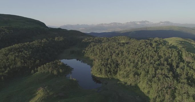 An Aerial view of forest, a lake, the sae and mountains with a snowy tip in Lapland in the Lofoten Islands in Norway.
