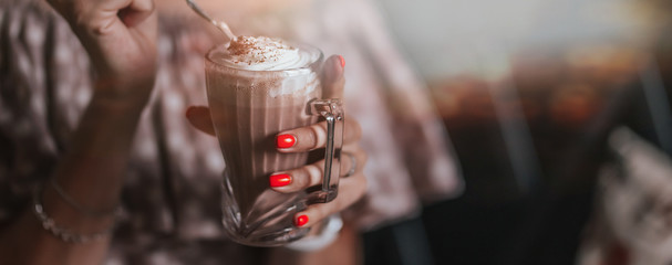 young woman sitting in cafe holding spoon ang glass with coffee or milkshake with whipped cream