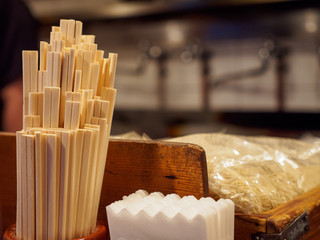Closeup detail of multiple disposable bamboo chopsticks in a holder next to bags of noodles on a tabletop at a Ramen restauraunt. Nakano, Tokyo, Japan. Travel and cuisine. - 289518988