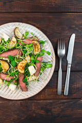 Green salad with steak, aubergine, sunflower sprouds and feta chese in ceramic plate on wooden background