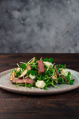 Green salad with steak, aubergine, sunflower sprouds and feta chese in ceramic plate on wooden background