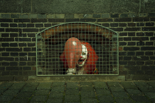 a scary clown with a balloon caged behind a lattice