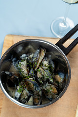 Top view of boiled mussels with herbs and garlic sauce in a pot with a glass of white wine and crunchy croutons
