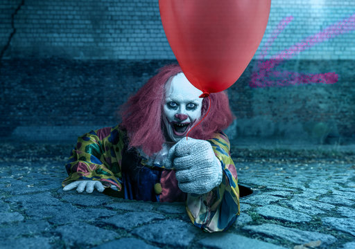 scary clown with a balloon rising from the sewer