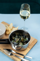 Boiled mussels with herbs and garlic sauce in a pot with a glass of white wine and crunchy croutons