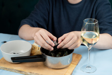 Man is eating boiled mussels with herbs with a glass of white wine and crunchy croutons