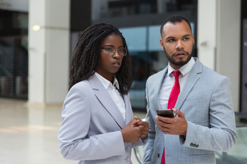 Serious businessman and businesswoman with smartphone. Confident young African American business people standing together and using mobile phone. Connection concept