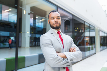 Confident young businessman looking at camera. Professional businessman standing with crossed arms and looking at camera outside office building. Business concept