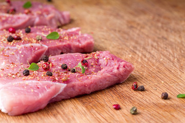 Raw pork steaks sprinkled with spices and herbs. Juicy raw steaks for a barbecue, close up.