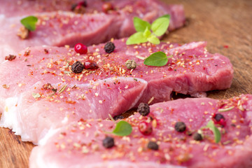 Raw pork steaks sprinkled with spices and herbs. Juicy raw steaks for a barbecue, close up.