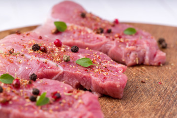 Raw pork steaks sprinkled with spices and herbs. Juicy raw steaks for a barbecue, close up.