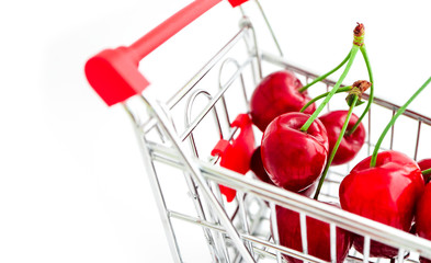 Shopping trolley basket with a fresh red cherries, isolated on white background. Food consumption,...