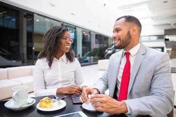 Diverse office friends enjoying coffee hour together. Business man and woman sitting in cafe, talking and laughing. Coffee break concept