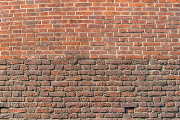 Old brickwork. The wall is made of red brick. The upper part of the wall is a lighter color. The bottom of the wall is darker in color.
