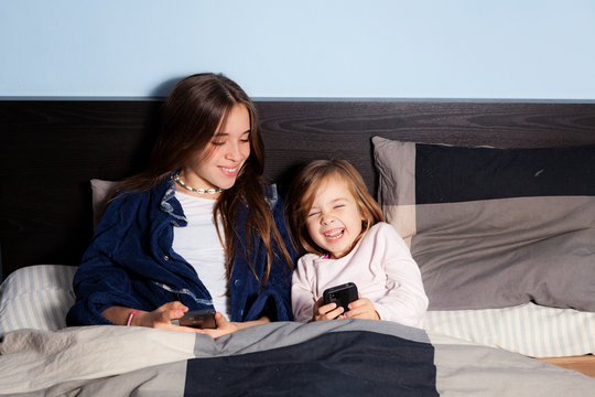 two sisters at bed in the morning playing with a smartphone