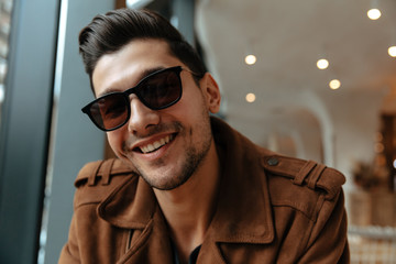 Man portrait. Cafe. Handsome young man in casual clothes and sunglasses is looking at camera and smiling while sitting in cafe